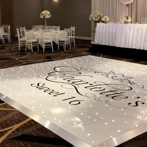 May include: A white dance floor with a black inscription that reads "Charlotte's Sweet 16" with a crown design. The floor is lit with small white lights.