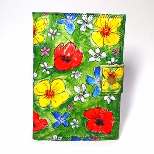 May include: A green floral journal with a button closure. The cover features a hand-painted design of yellow, red, blue, and white flowers on a green background. The journal is rectangular and has a stitched border.