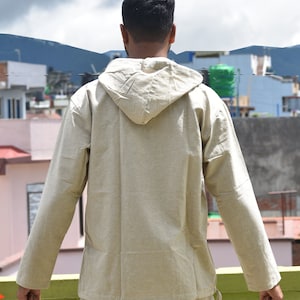 Pu&ograve; includere: Una camicia beige a maniche lunghe con cappuccio e coulisse sul fondo.