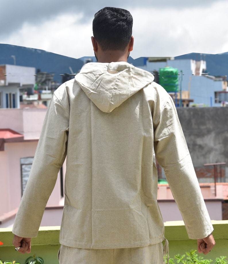Pu&ograve; includere: Una camicia beige a maniche lunghe con cappuccio e coulisse sul fondo.