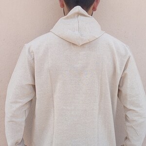 May include: A beige hooded long-sleeved shirt with colorful trim on the cuffs. The shirt is made of a soft, comfortable fabric.