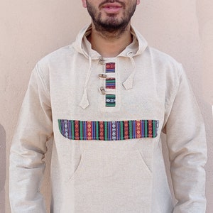 May include: A beige hooded sweatshirt with a colorful patterned band across the chest and matching trim on the sleeves. The sweatshirt has a kangaroo pocket and a drawstring hood.
