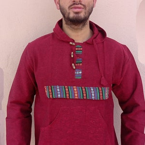 May include: A maroon hooded sweatshirt with a patterned band across the chest and a single wooden button closure. The sweatshirt has a large front pocket.