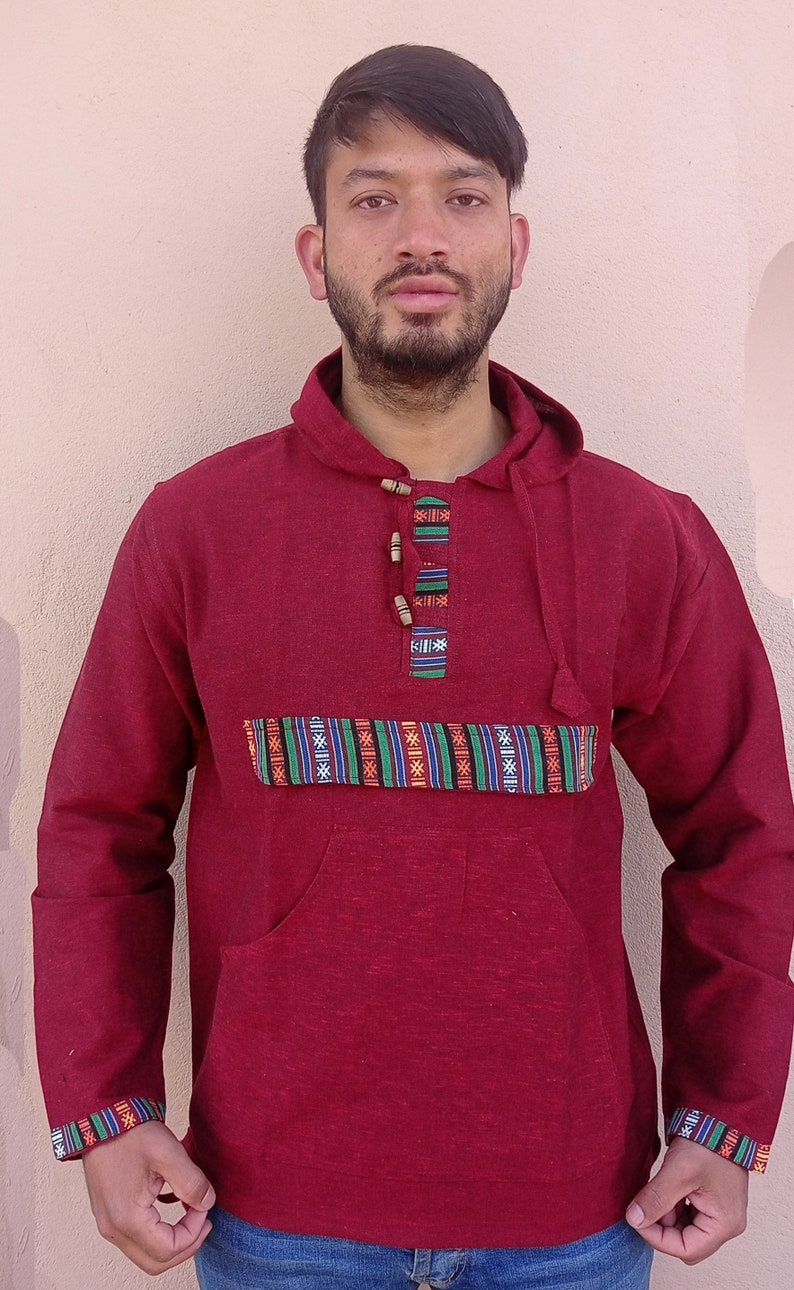 May include: A maroon hooded sweatshirt with a patterned band across the chest and a single wooden button closure. The sweatshirt has a large front pocket.