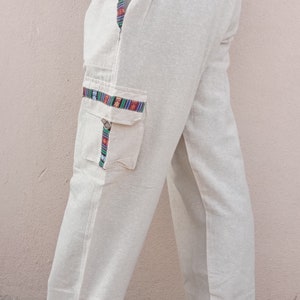 May include: Beige linen pants with a colorful patterned trim along the side seams and a large cargo pocket on the left leg.