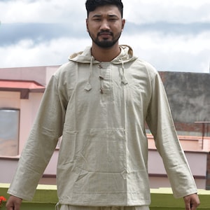Pu&ograve; includere: Una camicia beige con cappuccio a maniche lunghe e una tasca sul davanti. La camicia ha una chiusura con bottone al collo.