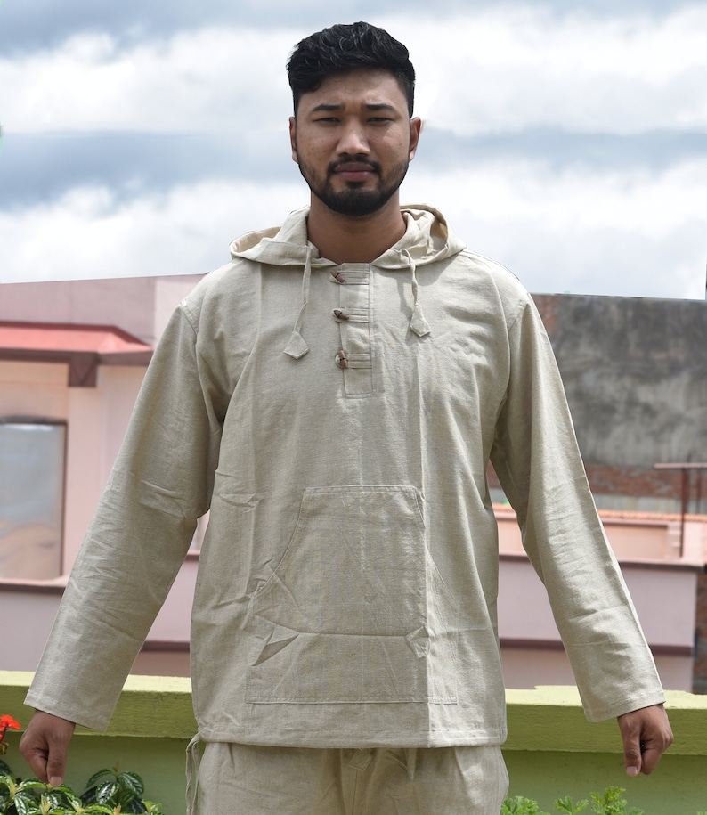 Pu&ograve; includere: Una camicia beige con cappuccio a maniche lunghe e una tasca sul davanti. La camicia ha una chiusura con bottone al collo.