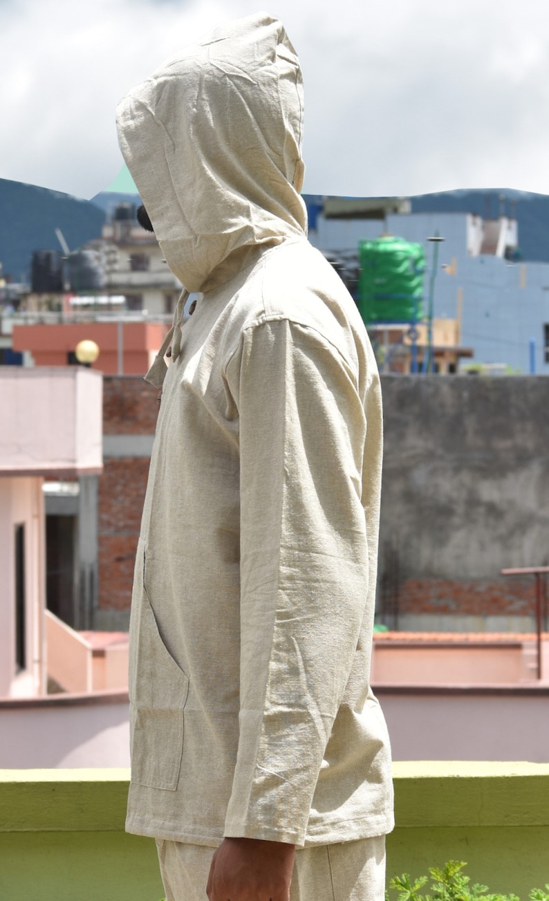 Pu&ograve; includere: Una camicia di lino beige con cappuccio, maniche lunghe e chiusura con bottoni. La camicia ha una vestibilit&agrave; rilassata e uno stile casual.