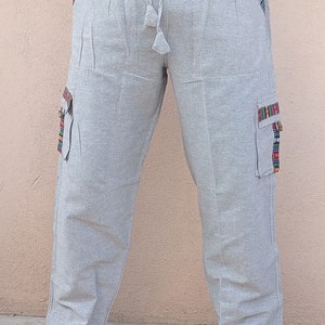 May include: Gray linen pants with a drawstring waist and side pockets. The pockets have colorful embroidered trim.