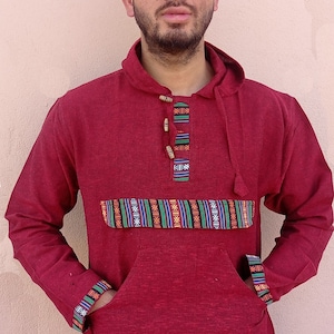 May include: A maroon hooded sweatshirt with a patterned band across the chest and a drawstring at the bottom. The sweatshirt has a kangaroo pocket and a button closure at the neck.