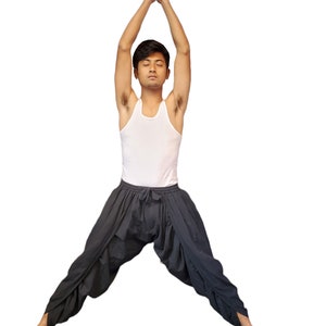 May include: A person wearing a white tank top and gray pants is doing a yoga pose with their arms raised above their head and their hands together in a prayer position.