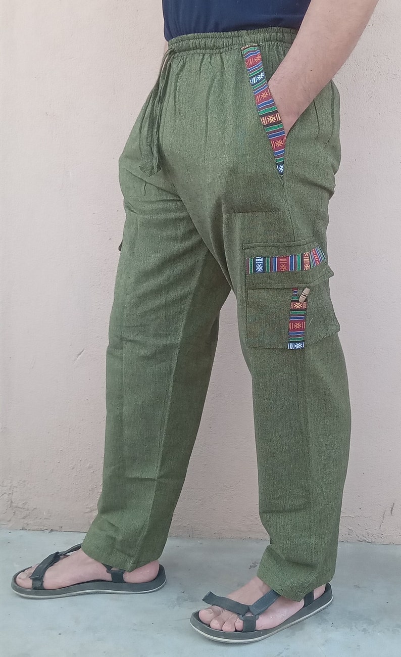 May include: Green cargo pants with a drawstring waist and colorful patterned trim. The pants have a large cargo pocket on the right leg with a flap and a decorative trim.