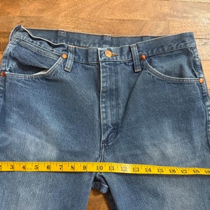 May include: Blue denim jeans with a straight leg cut. The jeans have a classic five-pocket design, copper rivets, and a button closure. A yellow measuring tape shows a length of approximately 20 inches.