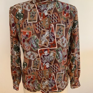Könnte beinhalten: Eine braune, langärmelige Bluse mit einem hohen Stehkragen. Die Bluse hat einen Druck mit Spielkarten mit verschiedenen Farben und Bildkarten.