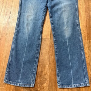 May include: Light blue denim jeans with a classic five-pocket design. The jeans have a straight leg cut and a faded wash, with visible wear marks. The stitching is a contrasting light color, and the jeans are made of a durable denim material.