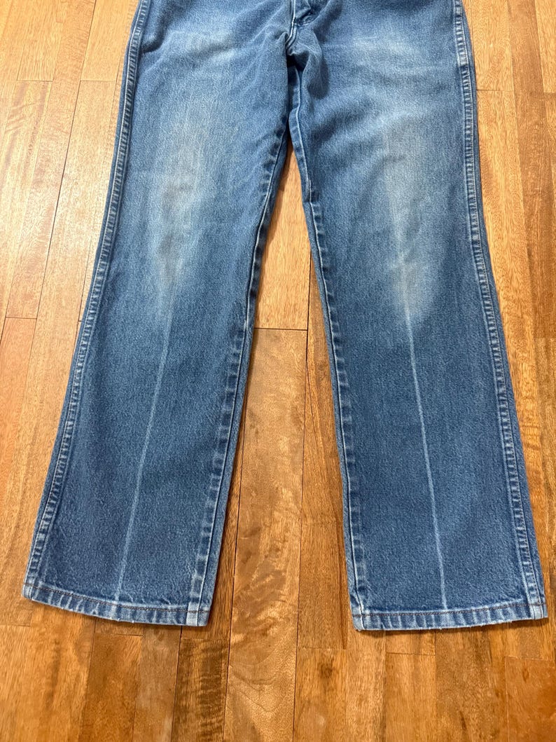 May include: Light blue denim jeans with a classic five-pocket design. The jeans have a straight leg cut and a faded wash, with visible wear marks. The stitching is a contrasting light color, and the jeans are made of a durable denim material.