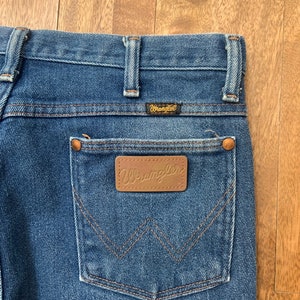 May include: Blue denim jeans with a brown leather patch that says "Wrangler" on the back pocket.