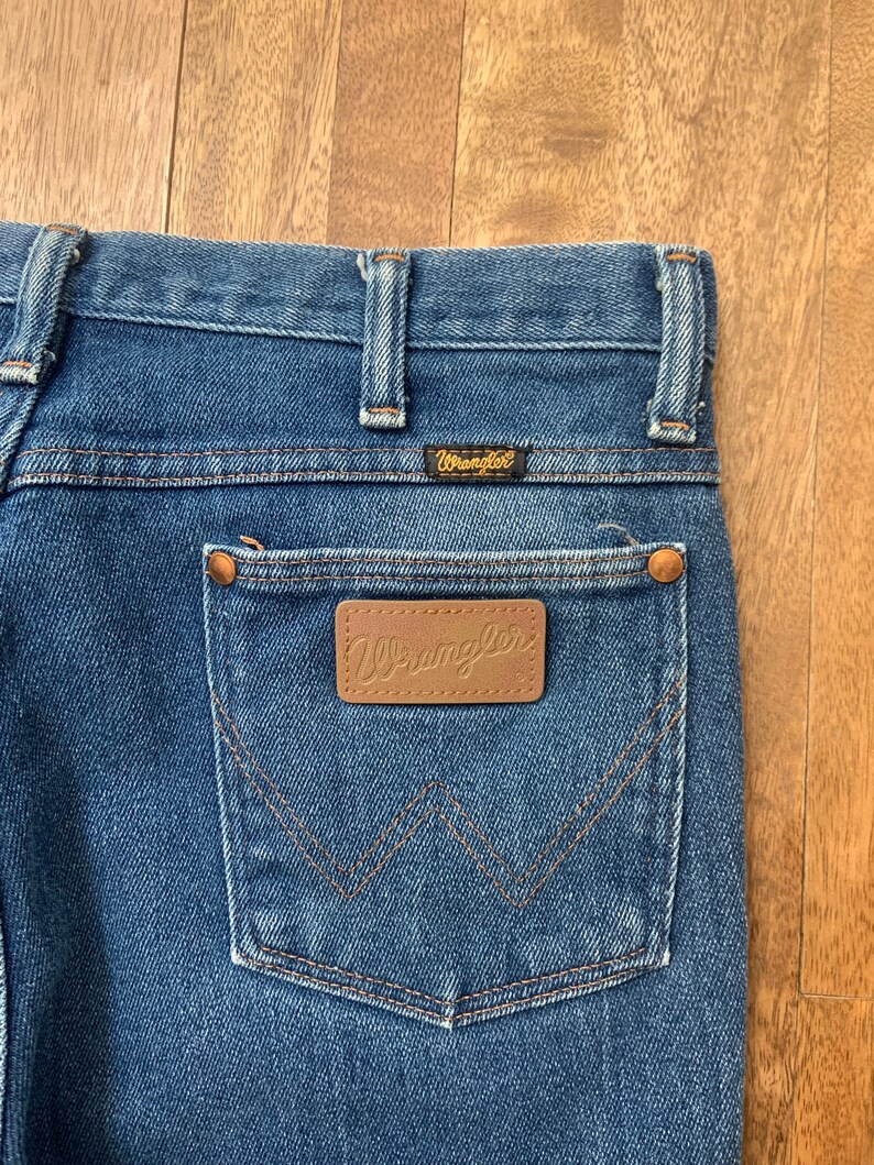 May include: Blue denim jeans with a brown leather patch that says "Wrangler" on the back pocket.