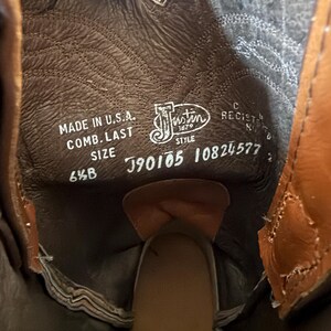 May include: Close-up of the inside of a brown leather cowboy boot. The boot's interior displays the brand name "Justin" and the text "Made in U.S.A.". The size is 6 1/2 B. The boot has a brown leather insole and a tan leather exterior.