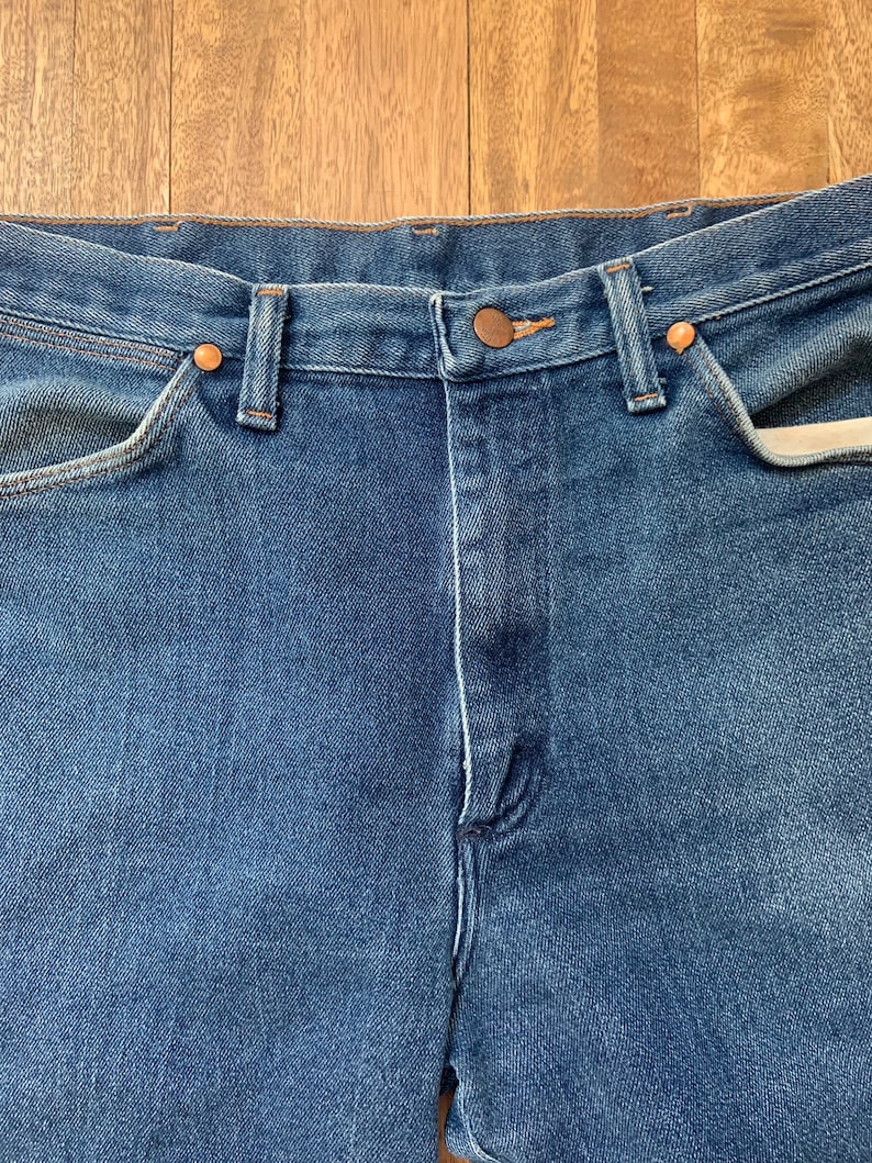 May include: A pair of blue denim jeans with a copper button and rivets. The jeans have a classic five-pocket style.