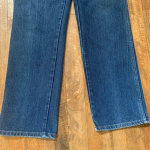 May include: A pair of blue denim jeans with a wide leg opening. The jeans are laying flat on a wooden surface.