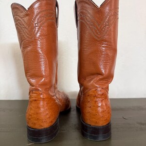 May include: A pair of brown cowboy boots. The boots have a textured leather appearance on the foot and a smooth leather upper with decorative stitching. The soles are dark brown, and the boots are set against a neutral background.