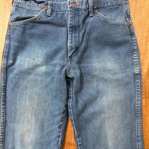May include: Blue denim jeans with a classic five-pocket design. The jeans have a faded wash and copper-colored rivets. The waist features a button closure and belt loops. The jeans are made of durable denim.