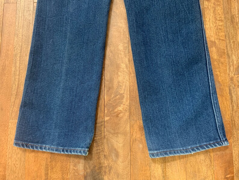 May include: Close-up of the bottom hems of a pair of blue denim jeans. The jeans have a straight leg style and are made of a soft, comfortable fabric.