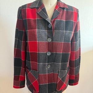 Könnte beinhalten: Ein rot-grauer karierter Blazer mit Knopfleiste und zwei aufgesetzten Taschen. Der Blazer hat einen klassischen Kragen und lange Ärmel.