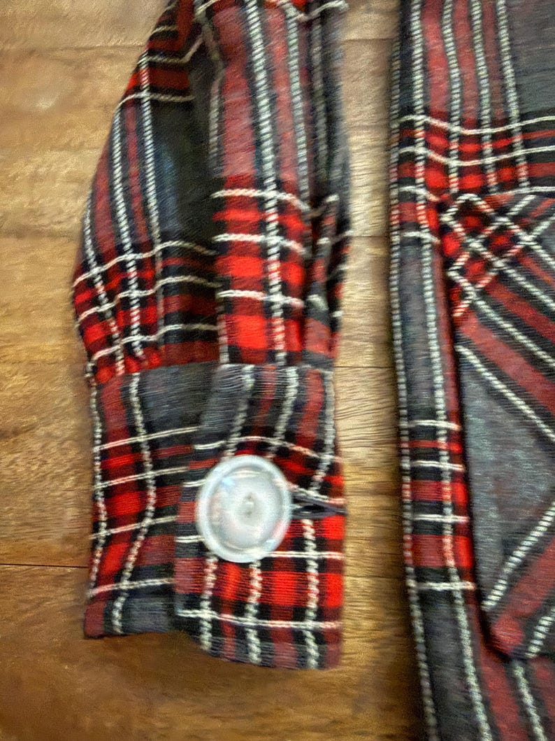 Może przedstawiać: Zbliżenie na rękaw koszuli w czerwoną, czarną i białą kratę. Mankiety zapinane na srebrny guzik. Wz&oacute;r koszuli to klasyczny tartan, z mieszanką czerwonych, czarnych i białych linii.
