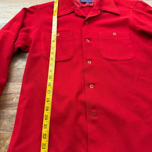 以下が含まれることがあります： 明るい赤色のボタンダウンシャツ。胸ポケットが2つ付いています。黄色のメジャーで約63.5cmの長さです。襟と長袖が付いています。「Pendleton」のブランド名がタグに表示されています。