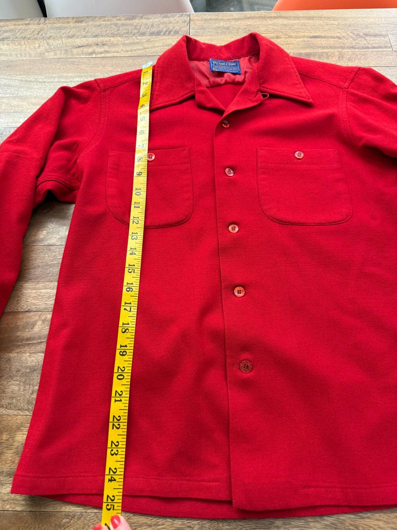 以下が含まれることがあります： 明るい赤色のボタンダウンシャツ。胸ポケットが2つ付いています。黄色のメジャーで約63.5cmの長さです。襟と長袖が付いています。「Pendleton」のブランド名がタグに表示されています。