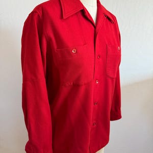 以下が含まれることがあります： 鮮やかな赤色のボタンダウンシャツ。胸ポケットが2つ、クラシックな襟が付いています。長袖シャツはマネキンに展示されており、その仕立ての良いフィット感と単色を強調しています。シャツには赤いボタンが付いています。