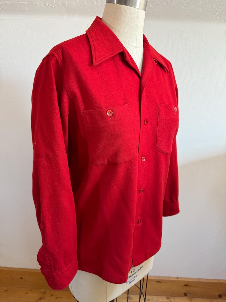 以下が含まれることがあります： 鮮やかな赤色のボタンダウンシャツ。胸ポケットが2つ、クラシックな襟が付いています。長袖シャツはマネキンに展示されており、その仕立ての良いフィット感と単色を強調しています。シャツには赤いボタンが付いています。