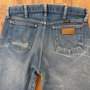 K&ouml;nnte beinhalten: Hellblaue Jeans aus Denim mit dem Wrangler-Logo auf der Ges&auml;&szlig;tasche. Die Jeans haben ein klassisches F&uuml;nf-Taschen-Design mit Kupfernieten und einem Lederaufn&auml;her. Die Ges&auml;&szlig;taschen haben die charakteristische Wrangler-Naht.
