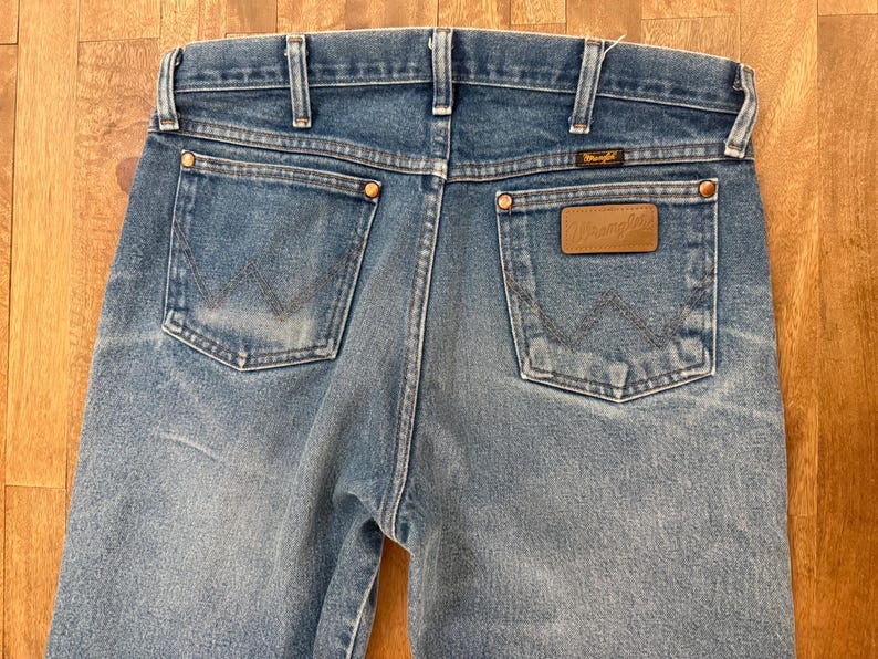 K&ouml;nnte beinhalten: Hellblaue Jeans aus Denim mit dem Wrangler-Logo auf der Ges&auml;&szlig;tasche. Die Jeans haben ein klassisches F&uuml;nf-Taschen-Design mit Kupfernieten und einem Lederaufn&auml;her. Die Ges&auml;&szlig;taschen haben die charakteristische Wrangler-Naht.
