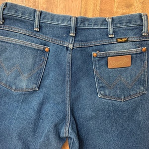May include: A pair of blue denim jeans with a brown leather patch on the back pocket that says "Wrangler".