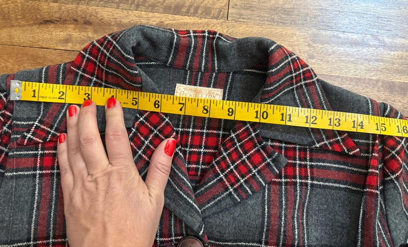 Może przedstawiać: Szara i czerwona kurtka w kratę z ż&oacute;łtą miarką na przodzie, pokazującą pomiar około 38 cm. Kurtka ma zapięcie na guziki i etykietę z napisem "Pendleton".