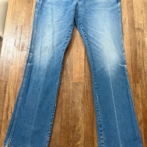 May include: Light blue denim jeans with a flared leg design. The jeans have a classic five-pocket style and a button and zipper closure. The denim has a faded appearance.