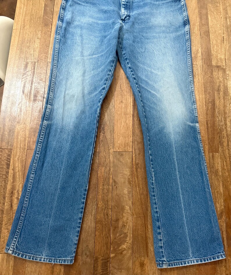 May include: Light blue denim jeans with a flared leg design. The jeans have a classic five-pocket style and a button and zipper closure. The denim has a faded appearance.
