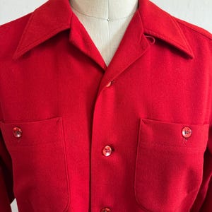 以下が含まれることがあります： 鮮やかな赤色のボタンダウンシャツ。胸ポケットが2つ、クラシックな襟が付いています。シャツにはお揃いの赤いボタンが付いています。生地は中程度の厚さで、涼しい季節に適しているようです。