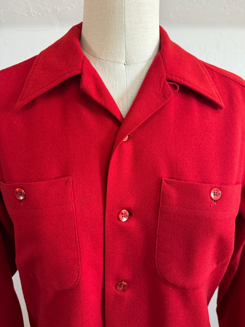 以下が含まれることがあります： 鮮やかな赤色のボタンダウンシャツ。胸ポケットが2つ、クラシックな襟が付いています。シャツにはお揃いの赤いボタンが付いています。生地は中程度の厚さで、涼しい季節に適しているようです。