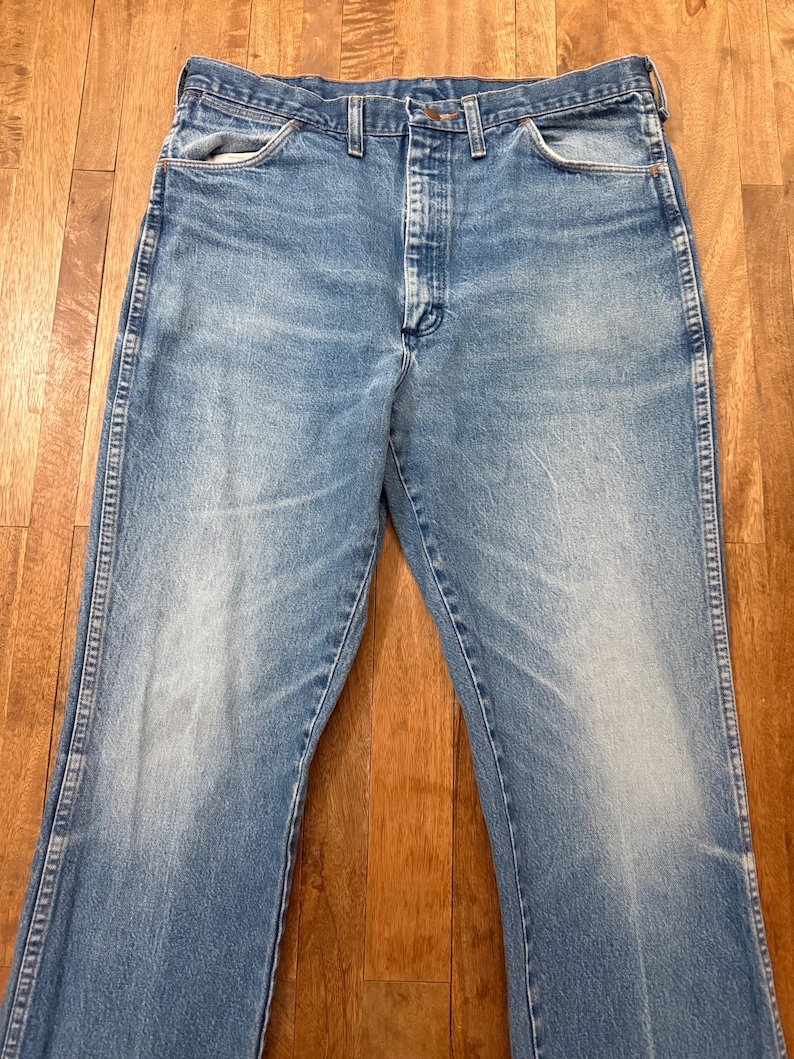 May include: Light blue denim jeans with a classic five-pocket design. The jeans have a faded wash and a straight leg fit. The jeans are made of durable denim material and feature a button and zipper closure.