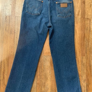 May include: A pair of blue denim jeans with a brown leather patch on the back pocket that says "Wrangler".