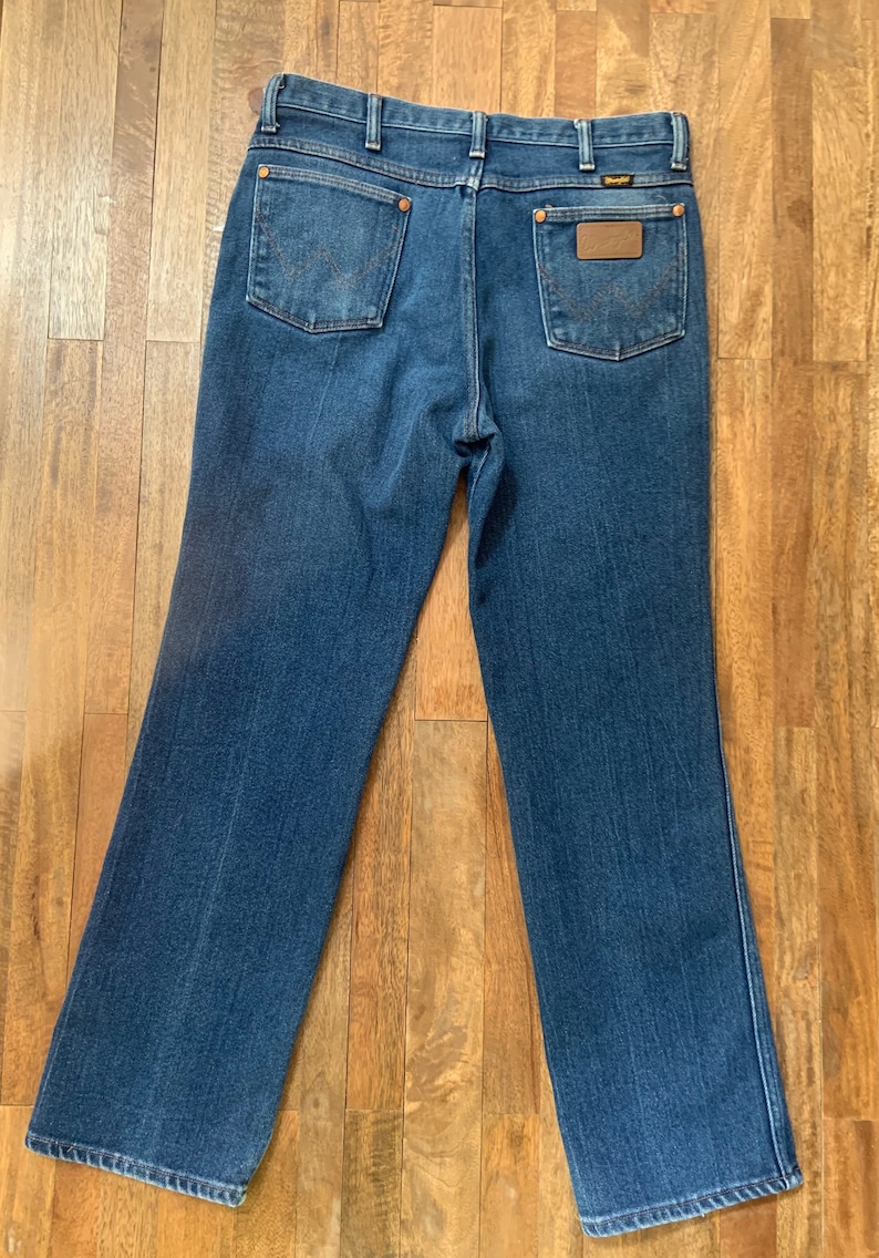 May include: A pair of blue denim jeans with a brown leather patch on the back pocket that says "Wrangler".