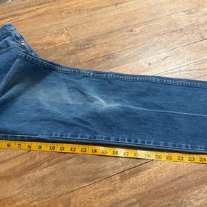 May include: Blue denim jeans with a yellow measuring tape laid across the leg. The jeans are folded and appear to be a size 34 waist. The measuring tape shows a length of approximately 30 inches.