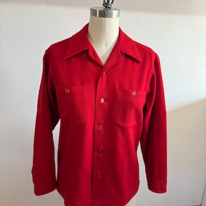 以下が含まれることがあります： クラシックな襟と2つの胸ポケットが付いた、鮮やかな赤色の長袖シャツ。 シャツはボタンダウンフロントで、マネキンに展示されています。 生地は中程度の重さの素材のようです。