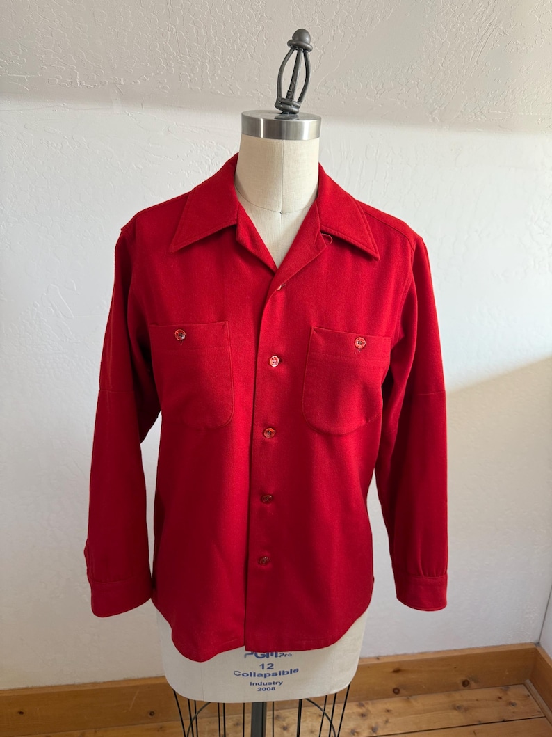 以下が含まれることがあります： クラシックな襟と2つの胸ポケットが付いた、鮮やかな赤色の長袖シャツ。 シャツはボタンダウンフロントで、マネキンに展示されています。 生地は中程度の重さの素材のようです。