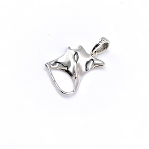 Puede incluir: Un colgante de plata con forma de manta raya. El colgante tiene un acabado liso y pulido y un bucle en la parte superior para sujetarlo a una cadena.