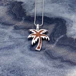 May include: A silver palm tree pendant necklace with a brown wood inlay. The necklace is on a silver chain.